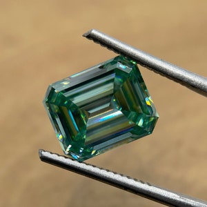 May include: A green emerald cut gemstone with a rainbow effect, held by tweezers.