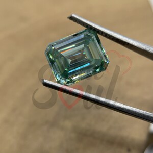 May include: A light green emerald cut gemstone with a high level of brilliance and fire. The gemstone is held in tweezers.