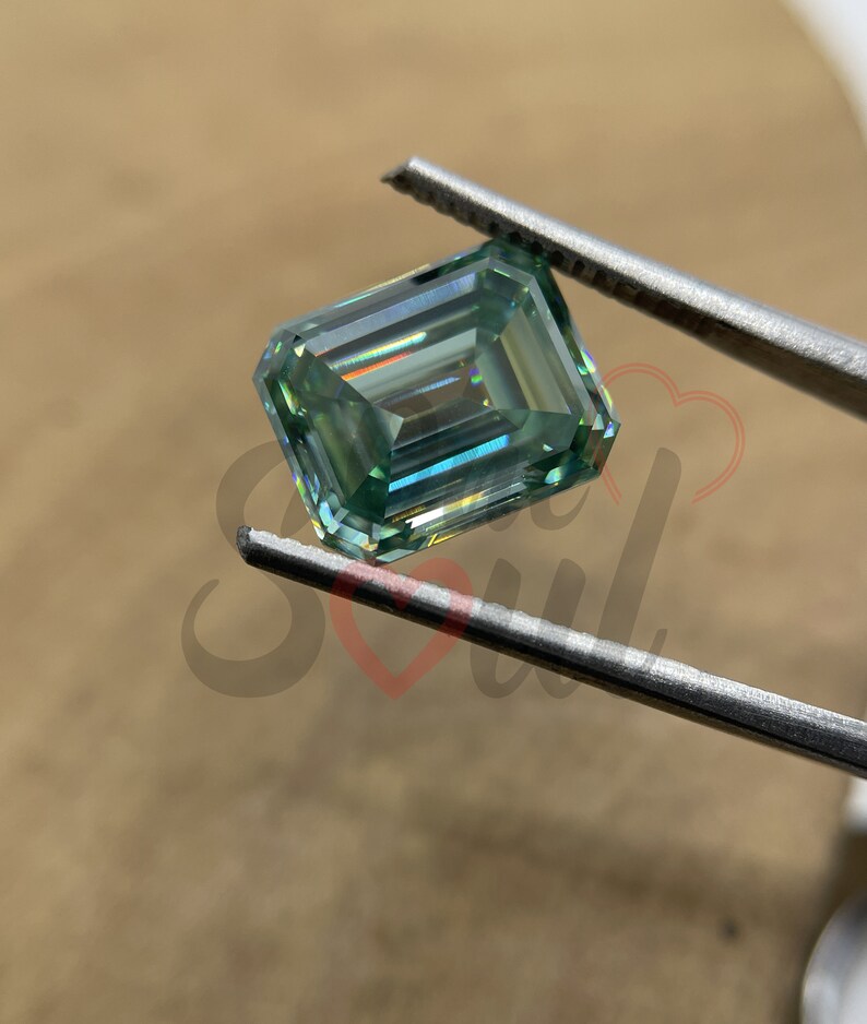 May include: A light green emerald cut gemstone with a high level of brilliance and fire. The gemstone is held in tweezers.