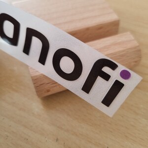 May include: A white sticker with black text that reads "anofi" with a purple dot. The sticker is on a wooden surface.