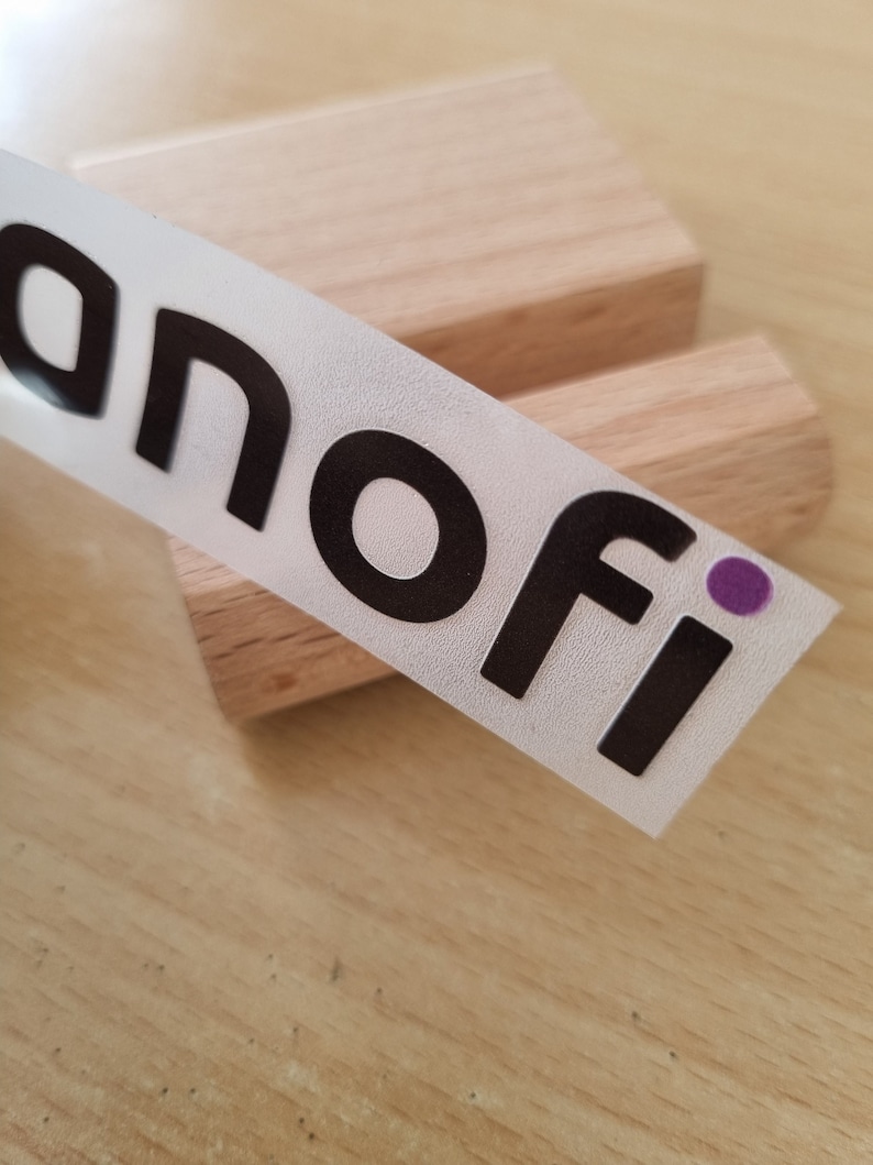 May include: A white sticker with black text that reads "anofi" with a purple dot. The sticker is on a wooden surface.