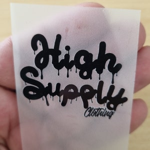 May include: A white heat transfer sheet with a black graphic that says "High Supply Clothing" in a dripping font.