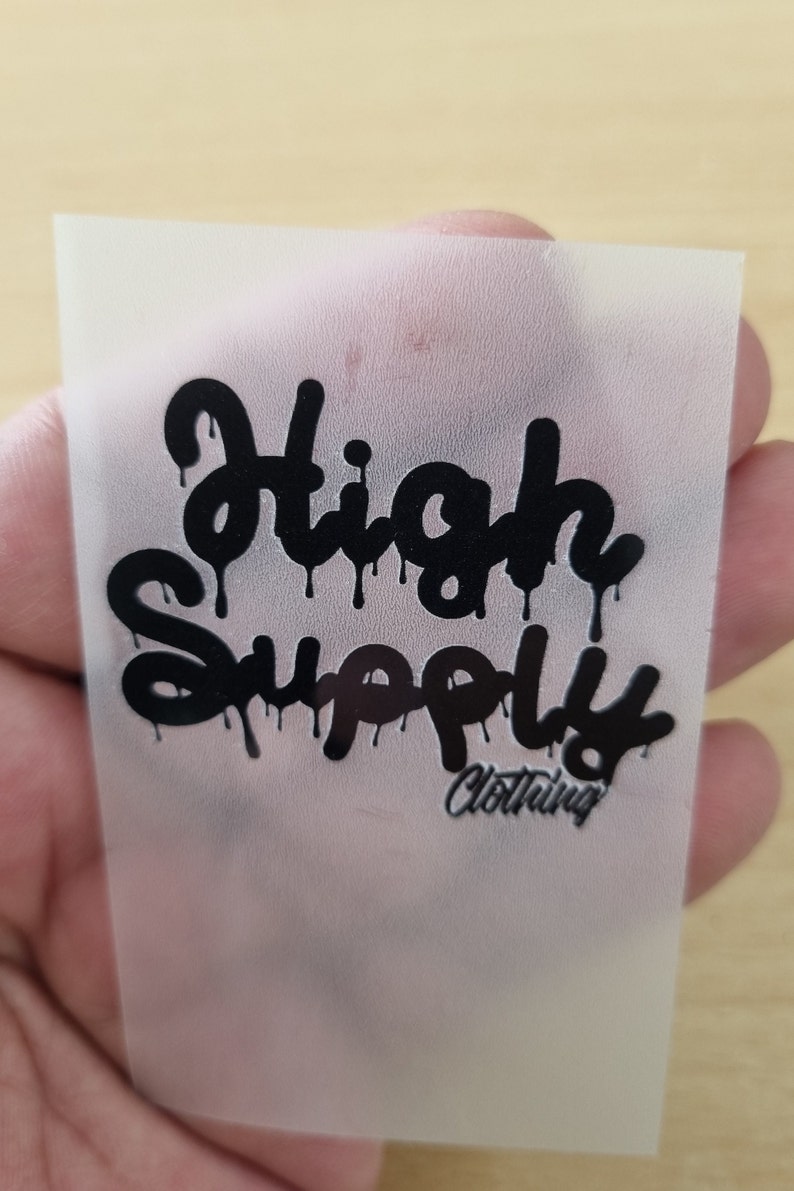 May include: A white heat transfer sheet with a black graphic that says "High Supply Clothing" in a dripping font.