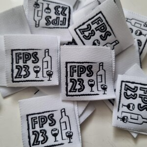 Pu&ograve; includere: Una collezione di etichette in tessuto bianco di forma quadrata con un disegno stampato in nero. Ogni etichetta mostra il testo FPS 23 accanto a una grafica di una bottiglia di vino e due calici, racchiusi in un bordo rettangolare disegnato.