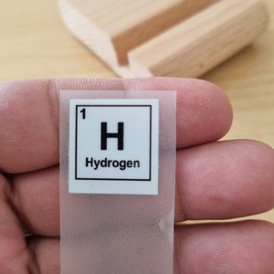 May include: A white sticker with a black border and the text "1 H Hydrogen" inside.