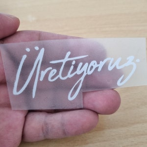 May include: A clear plastic sheet with the word "&Uuml;retiyoruz" written in white lettering.