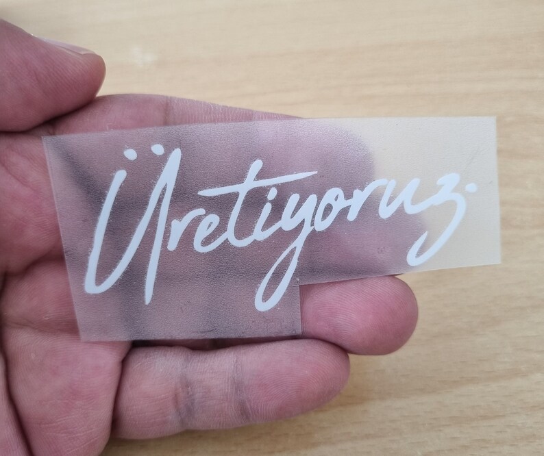 May include: A clear plastic sheet with the word "&Uuml;retiyoruz" written in white lettering.