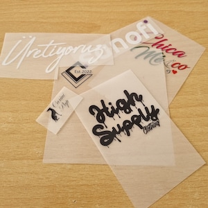 May include: Five iron-on heat transfer vinyl designs on clear sheets. The designs include "High Supply Clothing", "Cavini Pup", "&Uuml;retiyoruz", "znofi", and "Me & Chica Co."