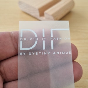 May include: A clear, frosted sticker with the text "DRIP'D IN FASHION - BY DYSTINY ANIQUE" in white lettering.