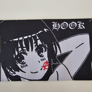 Pu&ograve; includere: Una toppa ricamata rettangolare raffigurante un personaggio in stile anime in bianco e nero con capelli corti. Il testo "HOOK" appare nell'angolo in alto a destra. Il personaggio ha le parole "book" e "fall" sulle guance, con un simbolo anarchico rosso.