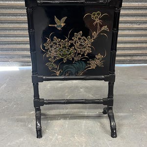 May include: Black decorative screen with a glossy finish, featuring a floral and bird design in gold and green. The frame has a bamboo-style design, with gold accents on the top. A unique piece for home decor.