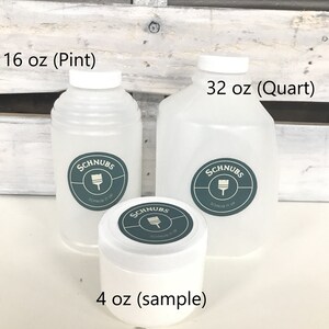 May include: Three white plastic containers of paint, labeled 16 oz (Pint), 32 oz (Quart), and 4 oz (sample). Each container has a white lid and a teal and white label with the text "SCHNUBS" and "SCHNUB IT UP".