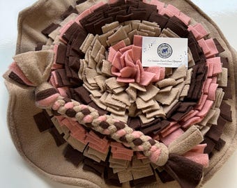 May include: A brown, pink, and beige dog toy with a braided rope attached. The toy is made of fleece and has a variety of textures. The toy is designed to help dogs engage their senses and keep them entertained.