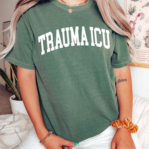 May include: A green t-shirt with the text "TRAUMA ICU" in white letters. The shirt is made of a soft, comfortable material and has a relaxed fit.