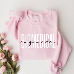 May include: A pink sweatshirt with the text "BIOMEDICAL engineer" in white letters with a black cursive font for the word "engineer".