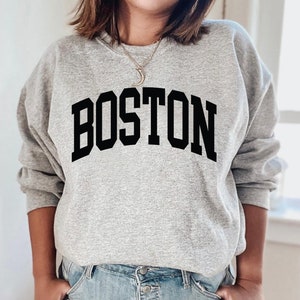 K&ouml;nnte beinhalten: Grauer Pullover mit schwarzem Text, der "BOSTON" in einer College-Schriftart lautet.