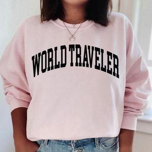 May include: A pink sweatshirt with the text "WORLD TRAVELER" printed in black.