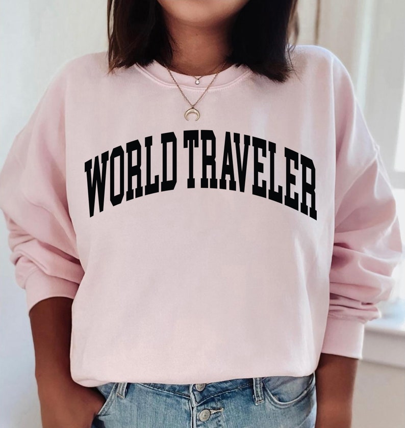 May include: A pink sweatshirt with the text "WORLD TRAVELER" printed in black.