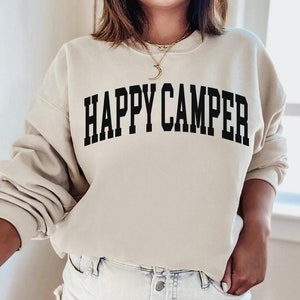 Peut inclure: Un sweat-shirt beige avec le texte "HAPPY CAMPER" imprim&eacute; en noir.
