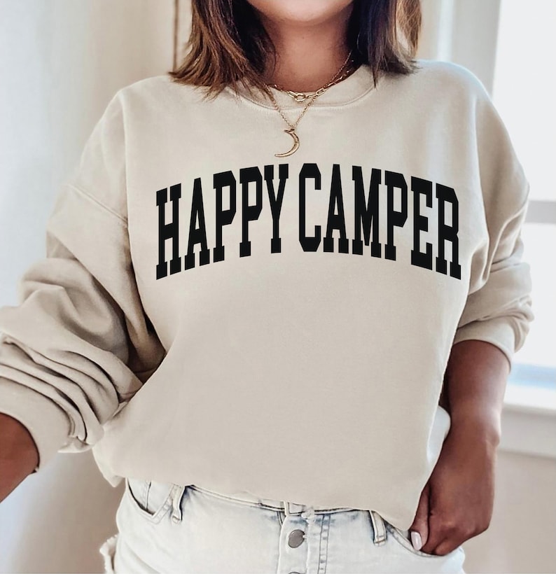 Peut inclure: Un sweat-shirt beige avec le texte "HAPPY CAMPER" imprim&eacute; en noir.
