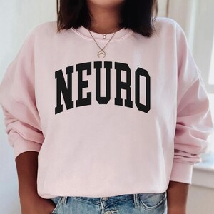 K&ouml;nnte beinhalten: Ein rosa Sweatshirt mit dem Wort "NEURO" in schwarzen Blockbuchstaben.