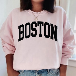 K&ouml;nnte beinhalten: Ein rosa Sweatshirt mit dem Wort "BOSTON" in schwarzen Blockbuchstaben.