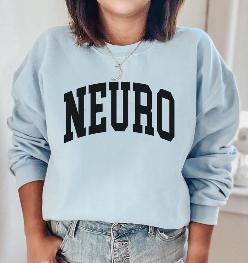 K&ouml;nnte beinhalten: Ein hellblauer Pullover mit dem Wort "NEURO" in schwarzer Schrift, in einer College-Schriftart.