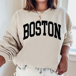 K&ouml;nnte beinhalten: Ein beiger Pullover mit dem Wort "BOSTON" in schwarzen Blockbuchstaben.