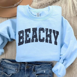 May include: Light blue sweatshirt with the word "Beachy" printed in black distressed lettering.