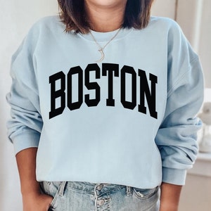 K&ouml;nnte beinhalten: Ein hellblauer Pullover mit dem Wort "BOSTON" in schwarzen Blockbuchstaben.