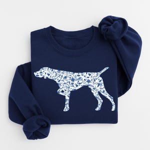 Op de afbeelding: Marineblauw sweatshirt met een wit silhouet van een hond gevuld met een blauw bloemenpatroon. De sweatshirt heeft een ronde hals en lange mouwen. Het hondenontwerp is gecentreerd op de voorkant van het kledingstuk.