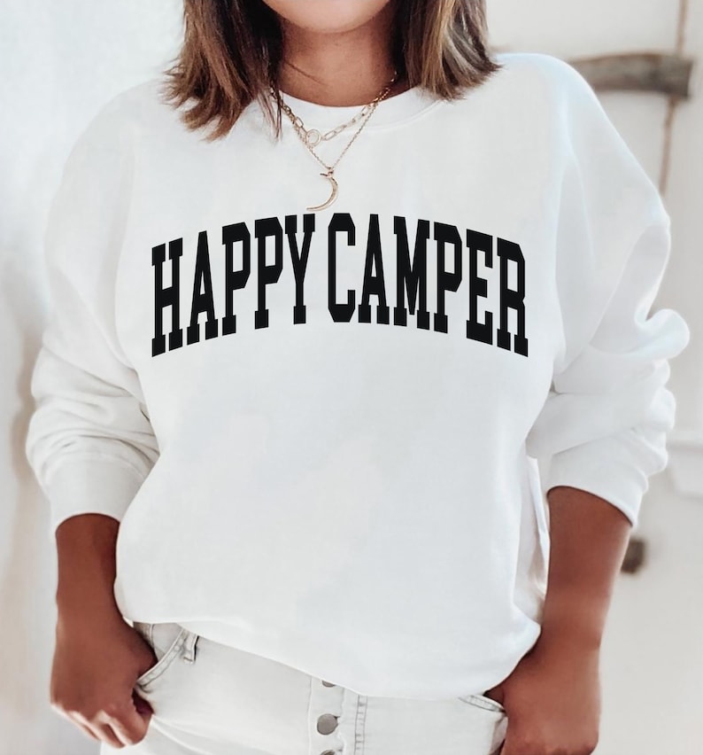 Peut inclure: Sweat-shirt blanc avec un texte noir qui dit "HAPPY CAMPER" dans une police d'&eacute;criture universitaire.
