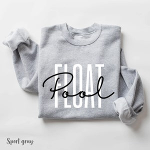 May include: A gray sweatshirt with the text "FLOAT Pool" printed in white letters with a black cursive "Pool" underneath.