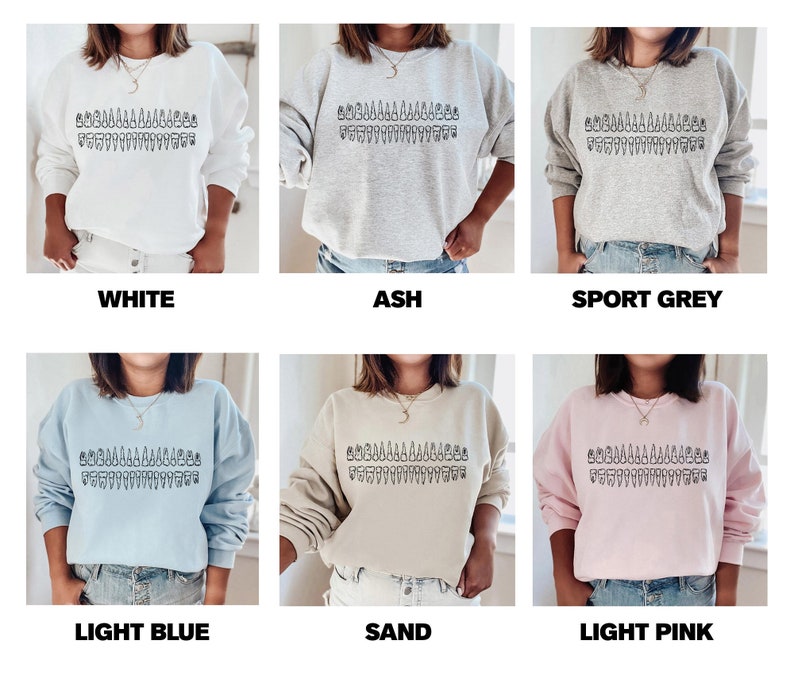 May include: A variety of colors of sweatshirts with a graphic of a row of trees on the front. The colors are white, ash, sport grey, light blue, sand, and light pink.