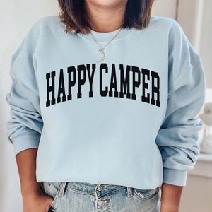 Peut inclure: Un sweat-shirt bleu clair avec le texte "HAPPY CAMPER" imprim&eacute; en noir.
