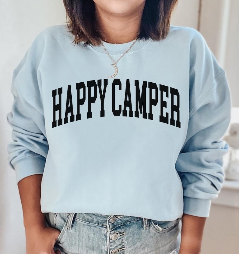 Peut inclure: Un sweat-shirt bleu clair avec le texte "HAPPY CAMPER" imprim&eacute; en noir.