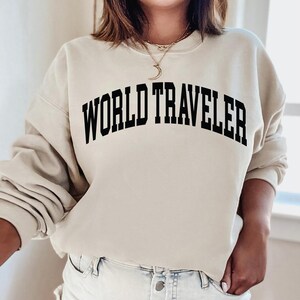 May include: A beige sweatshirt with the text "WORLD TRAVELER" printed in black across the front.