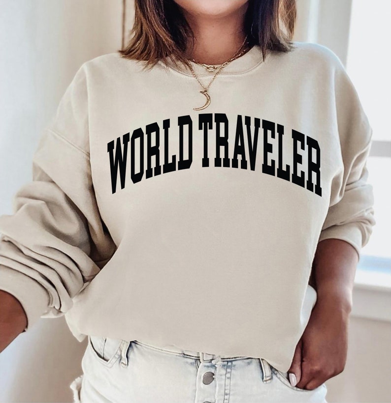 May include: A beige sweatshirt with the text "WORLD TRAVELER" printed in black across the front.