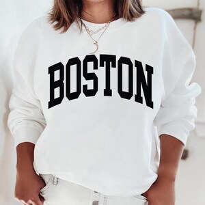 K&ouml;nnte beinhalten: Wei&szlig;er Pullover mit schwarzem Text, der "BOSTON" in einer College-Schriftart lautet.