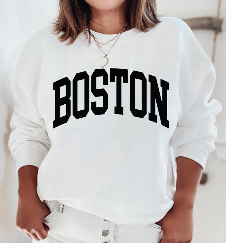 K&ouml;nnte beinhalten: Wei&szlig;er Pullover mit schwarzem Text, der "BOSTON" in einer College-Schriftart lautet.