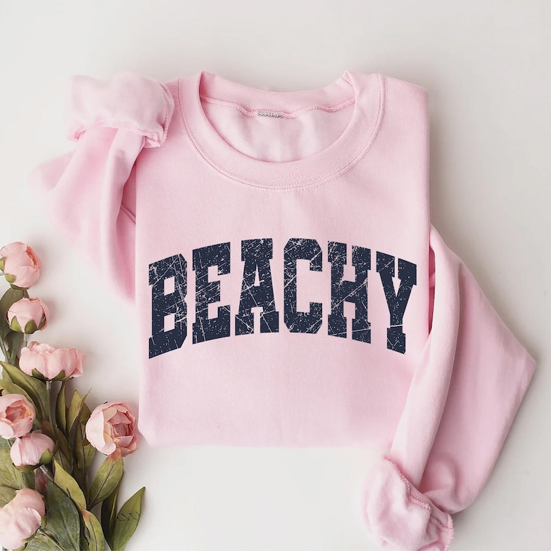 May include: A pink sweatshirt with the word "Beachy" printed in a navy blue, distressed font.