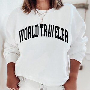 May include: White sweatshirt with black text that reads "WORLD TRAVELER" in an arched font.