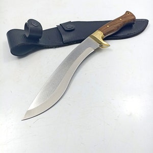 Puede incluir: Un cuchillo curvo de color plateado con mango de madera y funda de cuero negro. El cuchillo tiene una punta afilada y un borde dentado.