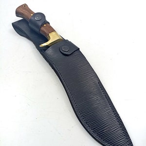 Puede incluir: Una funda de cuero negro con un cuchillo de mango de madera marr&oacute;n y hoja dorada.
