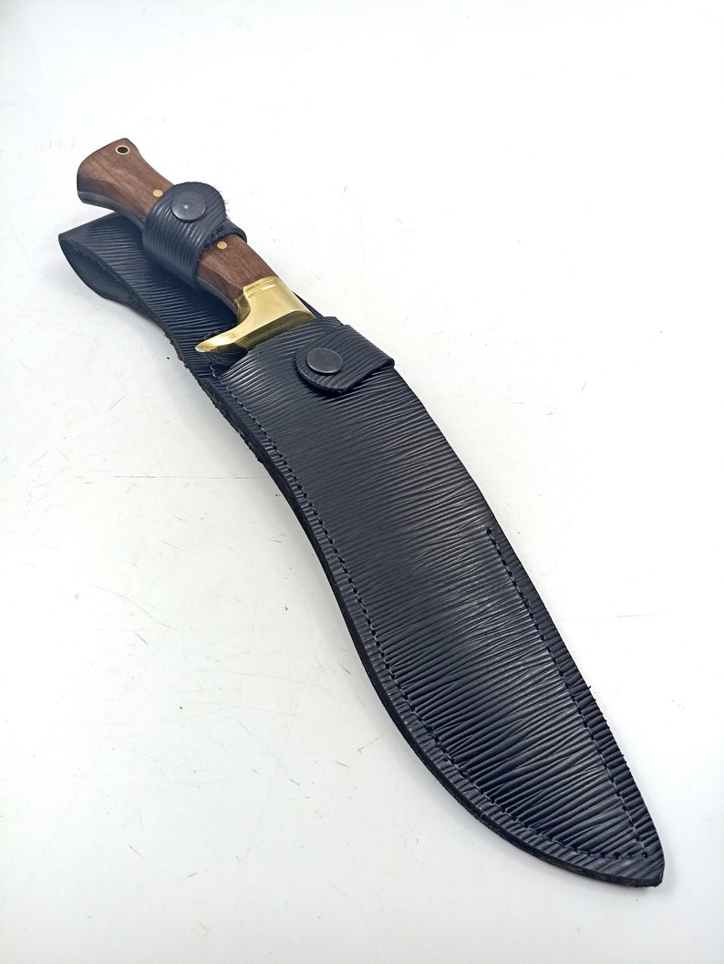 Puede incluir: Una funda de cuero negro con un cuchillo de mango de madera marr&oacute;n y hoja dorada.