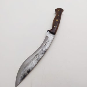 May include: A curved, silver-colored knife with a wooden handle. The handle has a brass inlay and a brass ring at the top.
