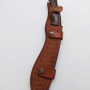 May include: A brown leather sheath with a decorative pattern and a brass snap closure. A wooden-handled knife is inside the sheath.