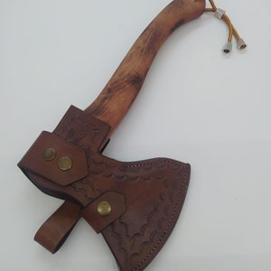 May include: A small axe with a wooden handle and a brown leather sheath. The axe head is covered by a brown leather sheath with decorative stitching and brass rivets. The wooden handle has a natural wood grain.
