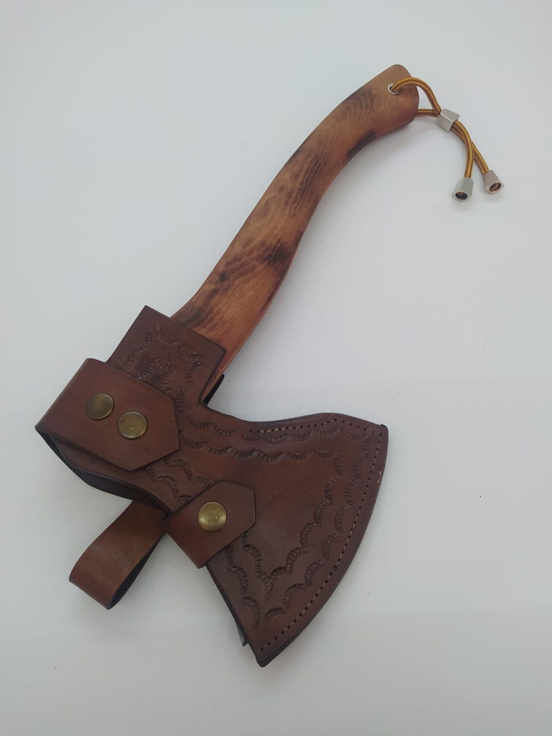 May include: A small axe with a wooden handle and a brown leather sheath. The axe head is covered by a brown leather sheath with decorative stitching and brass rivets. The wooden handle has a natural wood grain.