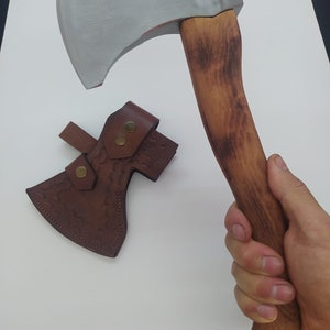 May include: Axe with a silver blade and a wooden handle. The handle is a light brown color. A brown leather sheath with a decorative pattern and two brass-colored snaps is included.